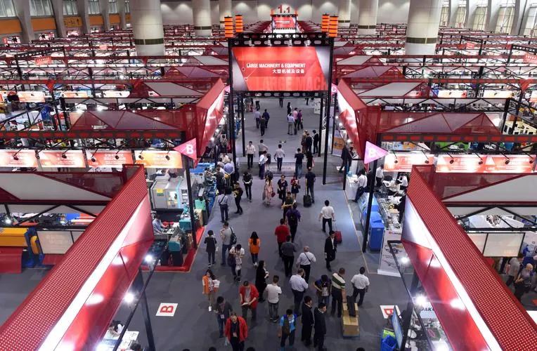 Visitors walking through a wide exhibition hall under red canopies in a machinery section.