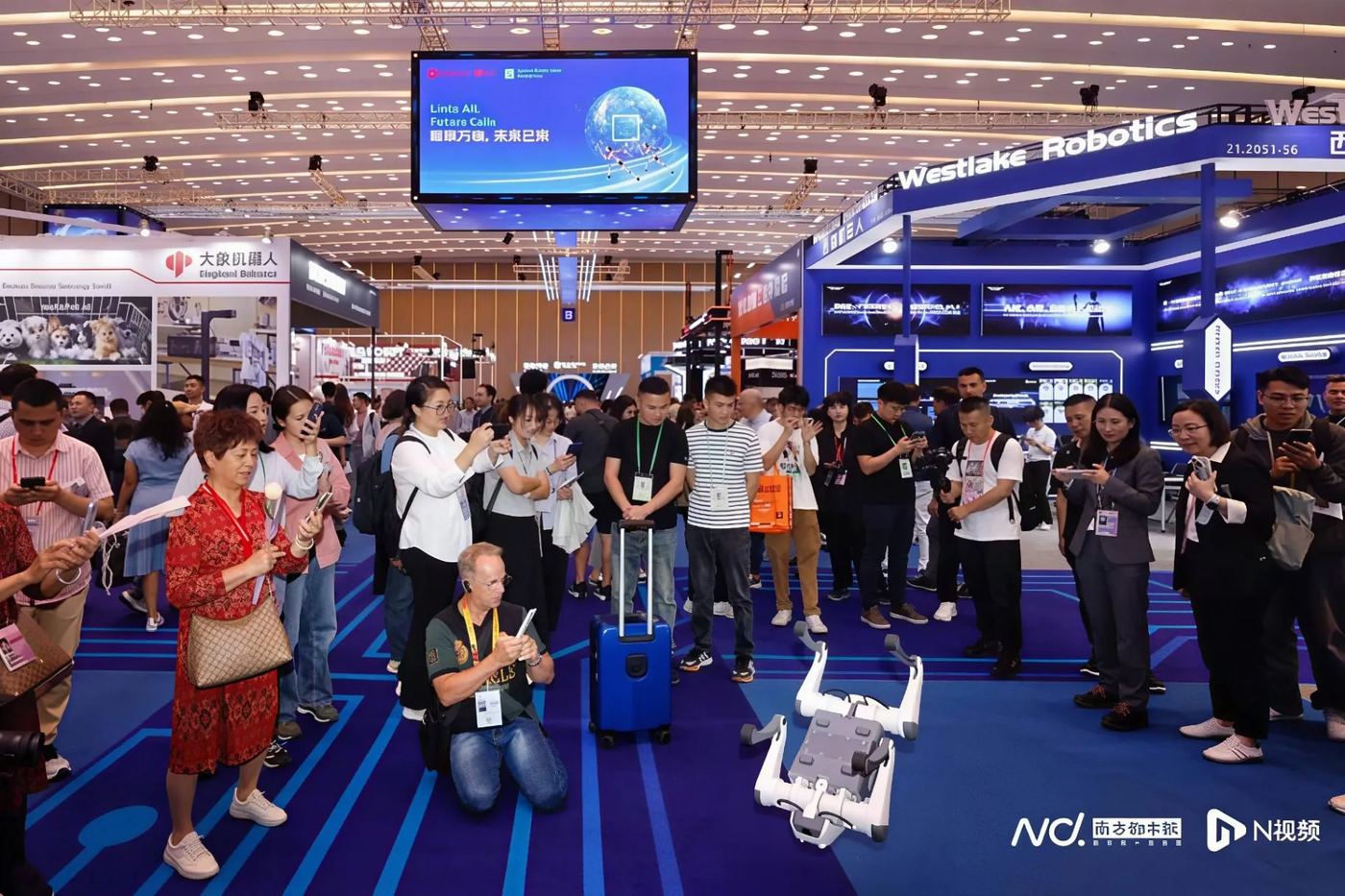 A quadruped robot performing in front of visitors holding up phones at a robotics booth.